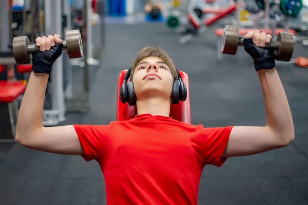 Photo young man in sports clothes and headphones is engaged with dumbbells in the gym