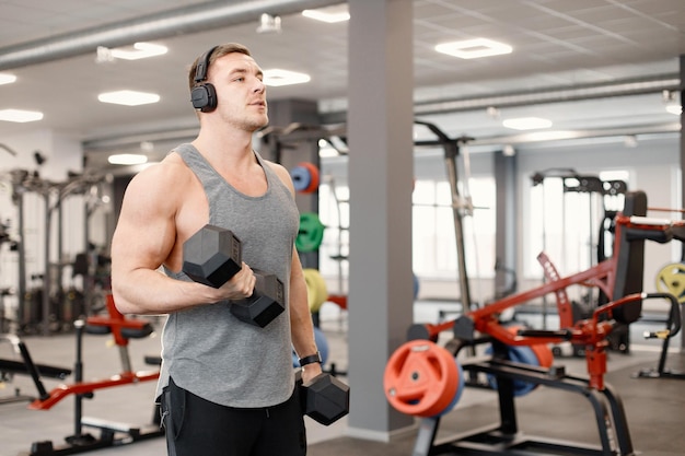 Young man in sportswear doing excercisses with dubells at gym