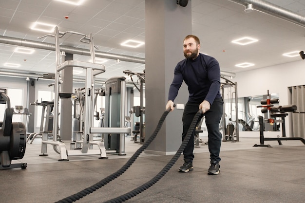 ジムで特別なロープでエクササイズをしているスポーツウェアの若い男