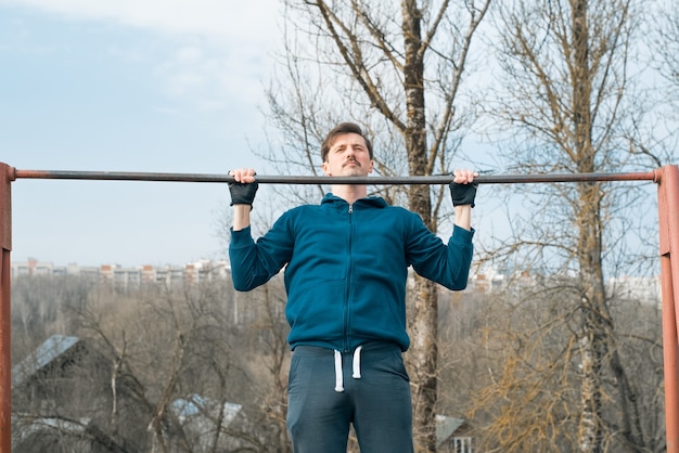 young man in sportswear exercising outside, pulling himself up on a horizontal bar