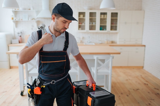 Photo young man stand in kitchen and look at toolbox in his hand