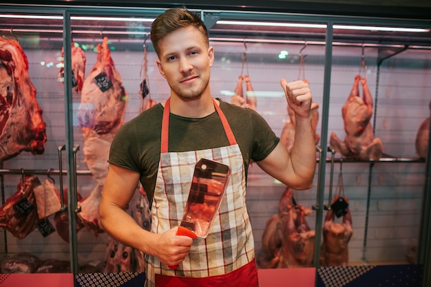 Photo young man stand and meat shelf in grocery store.