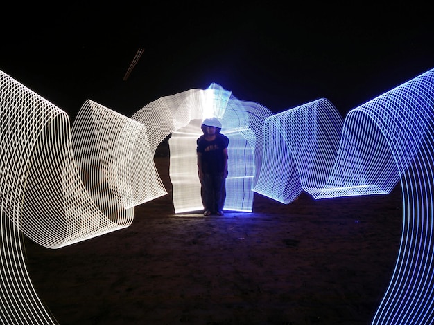 Foto giovane in piedi in mezzo a un dipinto luminoso sul campo di notte