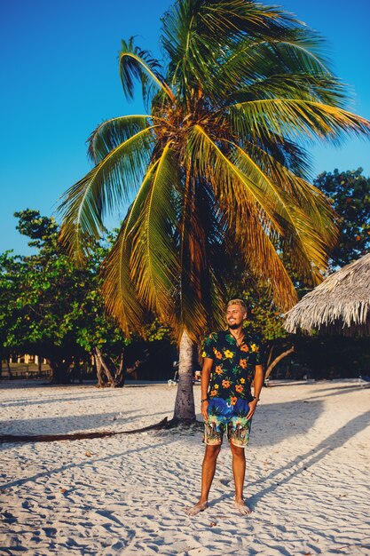 Молодой человек, стоящий на пляже, улыбаясь на фоне пальм