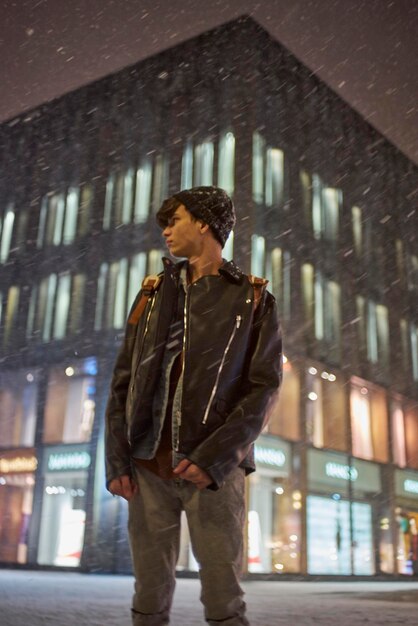 Young man standing in city at night during snowfall