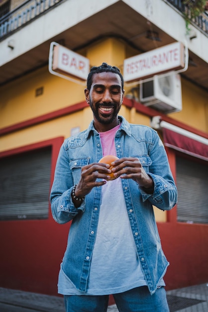 Young man standing eating a cheeseburger on the street