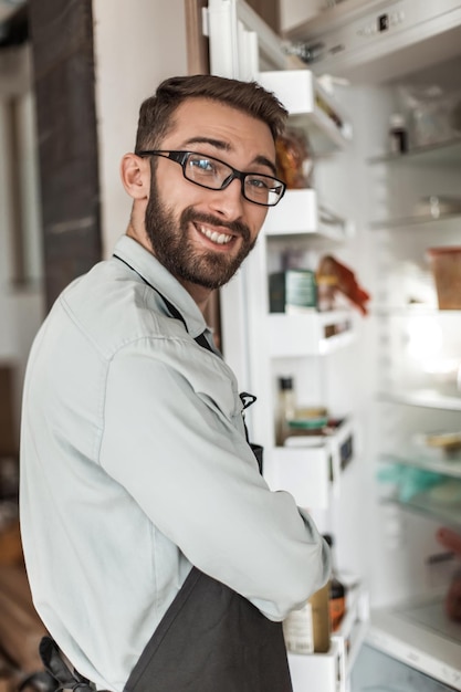 Молодой человек стоит возле открытого холодильника