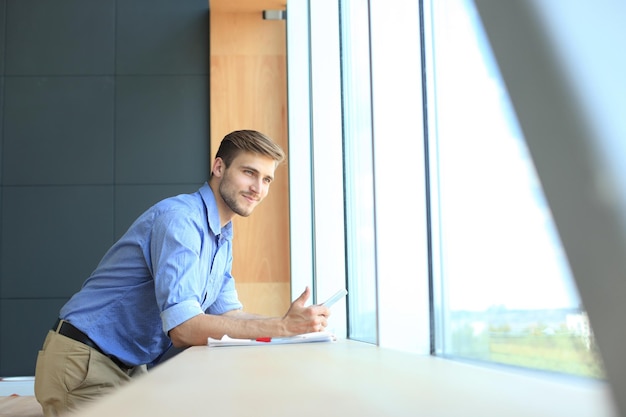 Young man standing near window in his office while thinking about his goals