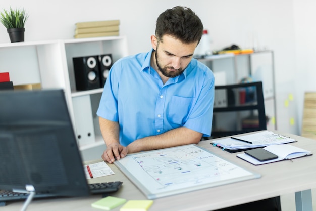 Foto un giovane uomo in piedi in ufficio a una scrivania del computer e lavorando con una lavagna magnetica.