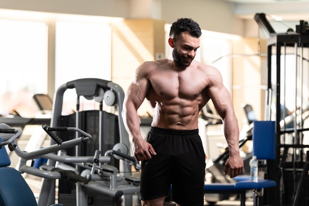 Young Man Standing Strong In The Gym And Flexing Muscles Muscular Athletic Bodybuilder Fitness Model Posing After Exercises