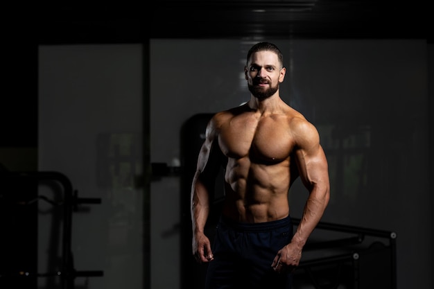 Young Man Standing Strong In The Gym And Flexing Muscles  Muscular Athletic Bodybuilder Fitness Model Posing After Exercises