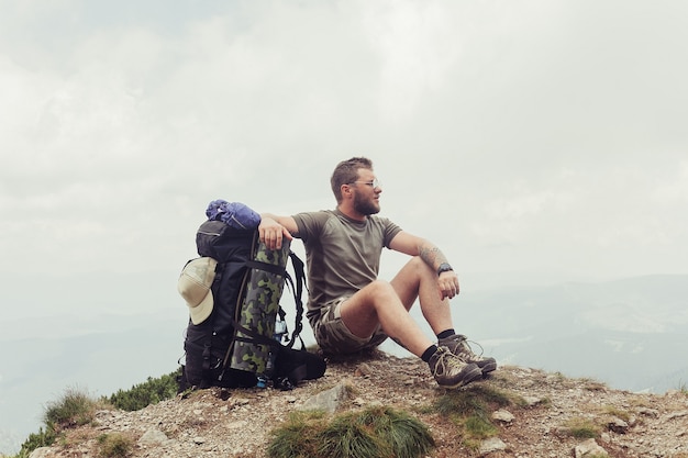 Young man standing on top of cliff in mountains enjoying view of nature