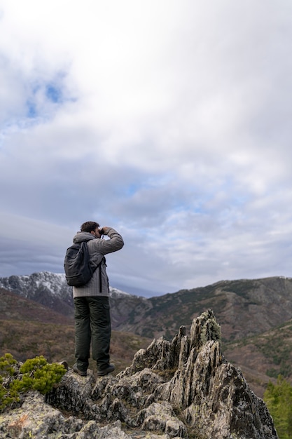 Young man standing on top of cliff in winter mountains at daytime