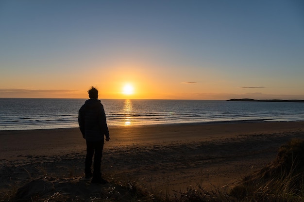 ビーチで夕日を見て立っている若い男