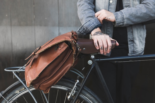 自転車に茶色のハンドバッグと立っている若い男