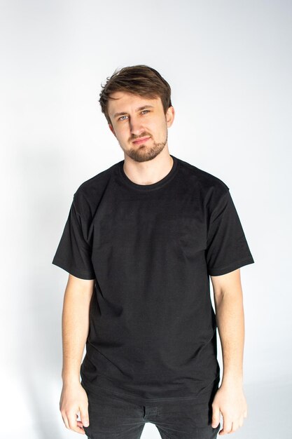 A young man stands in a black empty t-shirt and smiles