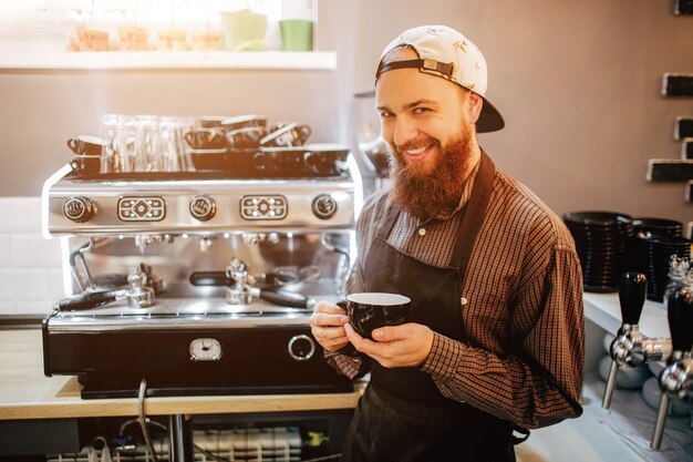 Young man stands at coffee machine and smile on camera