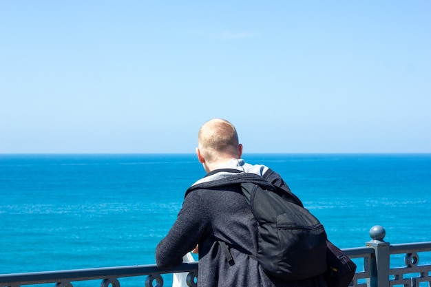 A young man stands on the embankment and looks at the sea