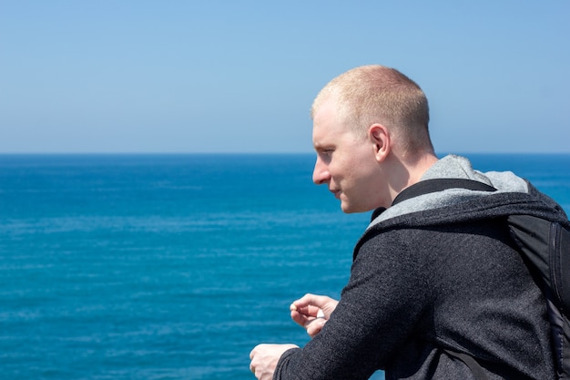 Молодой человек стоит на набережной и смотрит на море