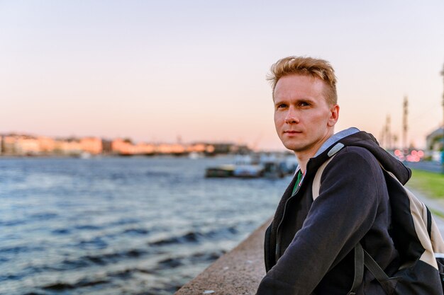 Photo a young man stands on the embankment in st petersburg at sunset