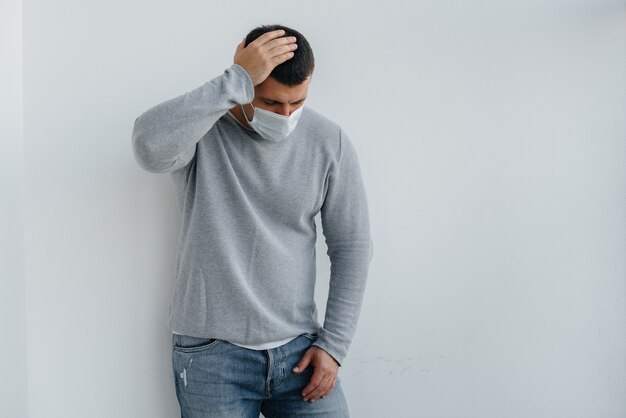 A young man stands on a gray wall wearing a mask during a quarantine