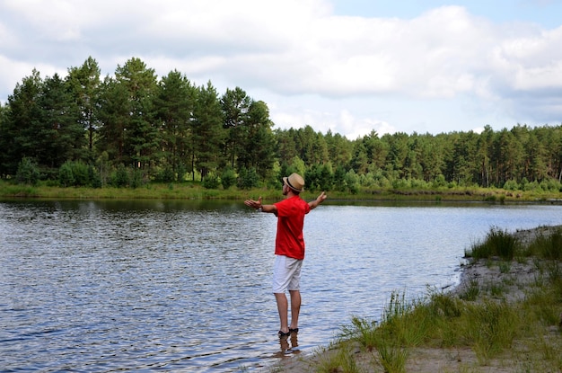 A young man stands on the shore of the lake with his arms outstretched