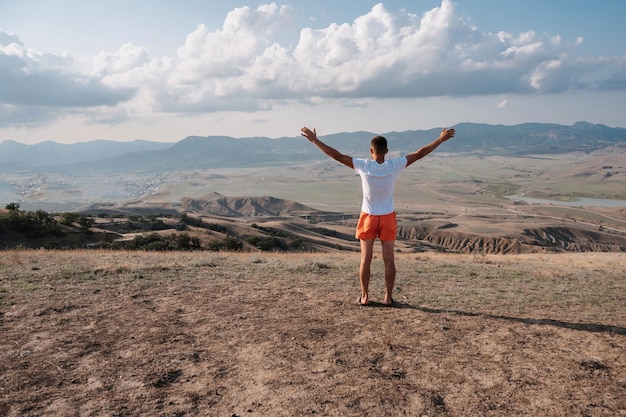 A young man stands with his hands up in the fresh air in a mountainous area. Place for your text.