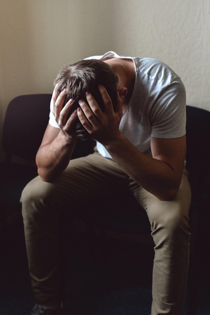 Photo a young man in a state of crisis and despair the white guy is sitting on a chair and holding his head with his hands