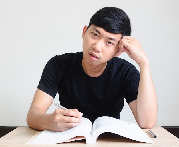 Young man strain and bored face with read the book on the desk on white isolated,Homework concept