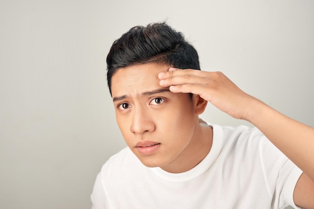 Young man struggling with acne on his face caring for his skin pushes acne