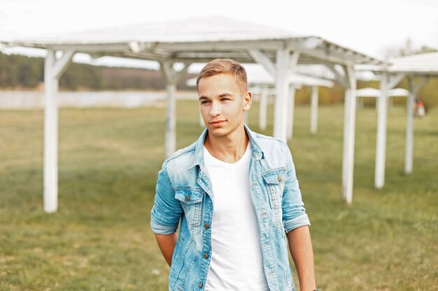 Photo young man in a stylish denim jacket and a white t-shirt is walking outdoors on a spring day