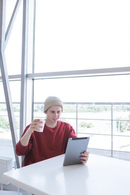 young man in a stylish dress sitting in a cafe with a glass of coffee and a tablet in his hands