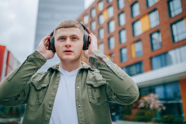 A young man in a stylish outfit headphones on listening to music and enjoying the beautiful city sky