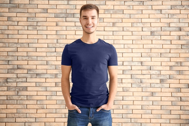 Young man in stylish t-shirt against brick surface. Mockup for design