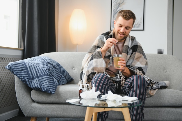 Young man suffering from cold at his home Shot of a young man sitting on his bed while feeling unwell at home Trying to stay warm Sick man