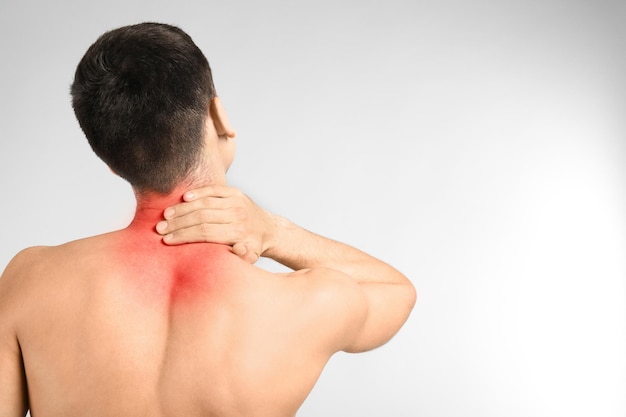 Young man suffering from neck pain on light background