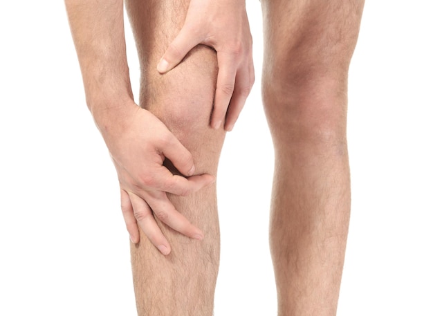 Young man suffering from pain in leg on white background closeup