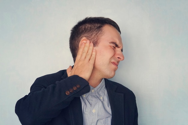 Young man suffering from Pain in right ear, over blue background. Medical concept. Diseases of the ear. Inflammation in the ear.