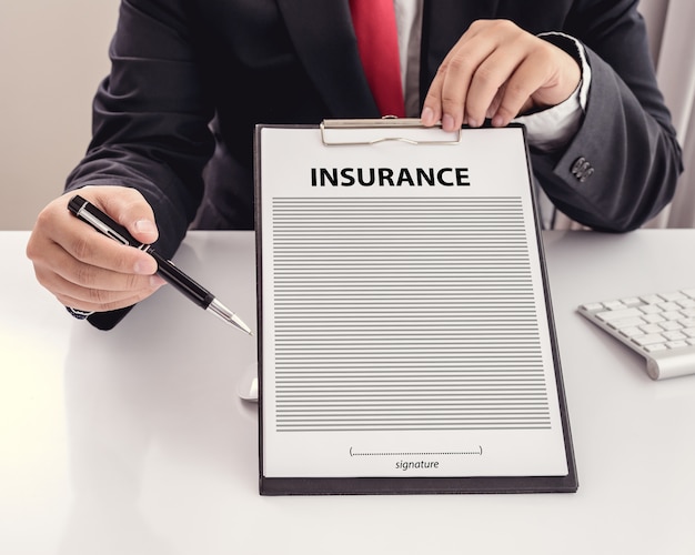 young man in suit in his office showing an insurance policy and pointing with a pen