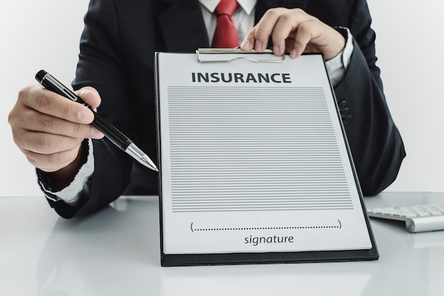 Photo young man in suit in his office showing an insurance policy and pointing with a pen