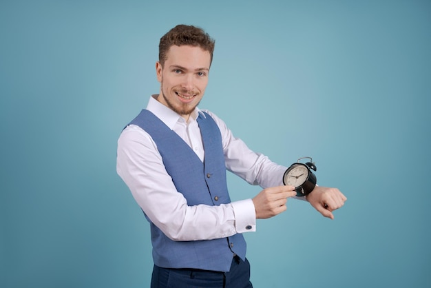 Young man in suit pointing at black alarm clock with his index finger Business