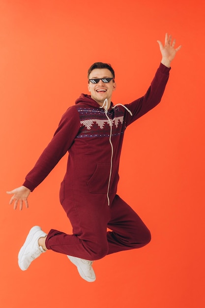 A young man in sunglasses and a Christmas kigurumi dances on a red background