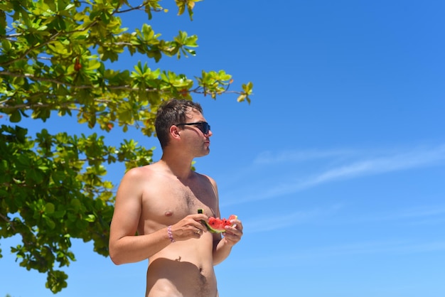 Young man in sunglasses eating a watermelon on a beach