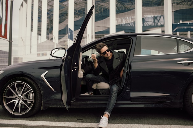 Young man in sunglasses getting out of car in town