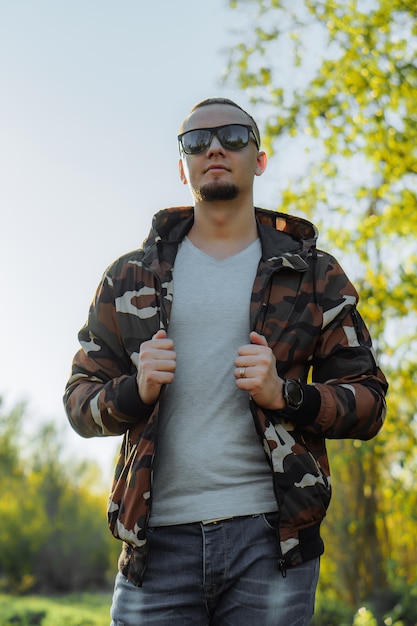 Photo young man in sunglasses and khaki jacket posing in park