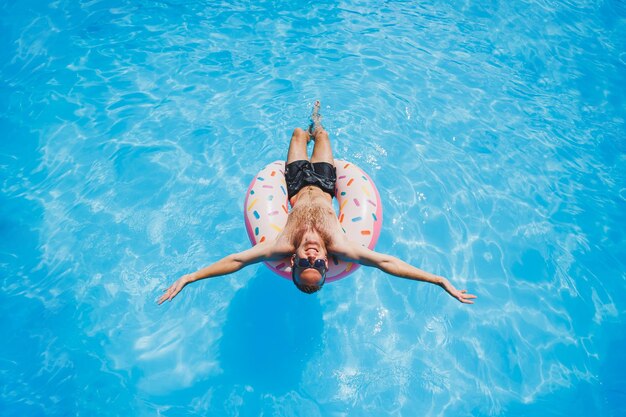 Un giovane in occhiali da sole e pantaloncini si sta rilassando su una ciambella gonfiabile in piscina vacanze estive