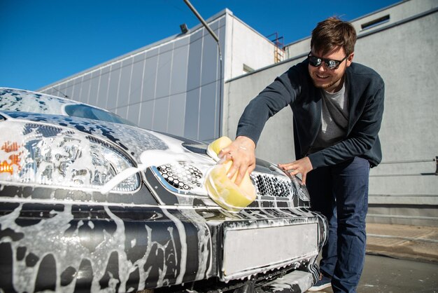 Young man in sunglasses washing car at self service carwash