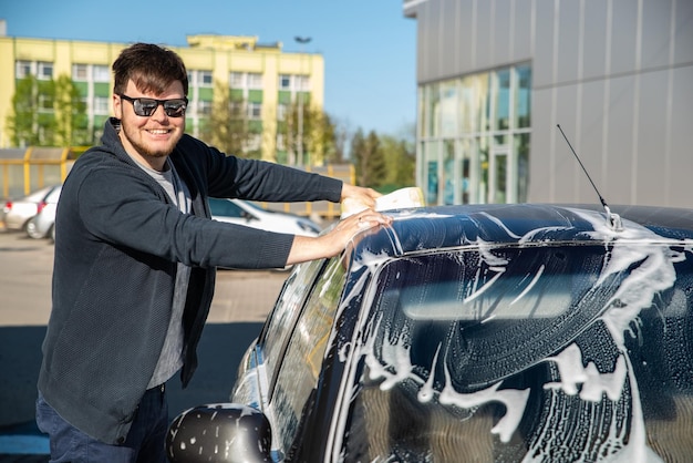 Young man in sunglasses washing car at self service carwash