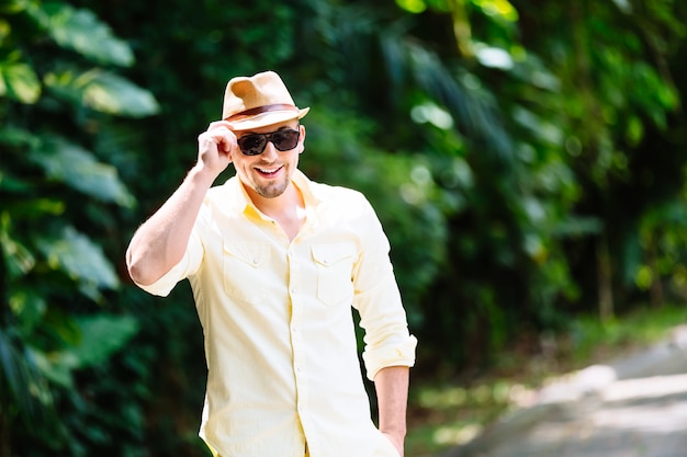 Giovane in occhiali da sole che portano cappello giallo e abbigliamento casual divertendosi nel giorno soleggiato. sfondo tropicale.