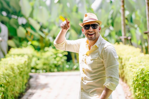 Young man in sunglasses wearing yellow hat and casual clothes having fun in sunny day. Tropical background.